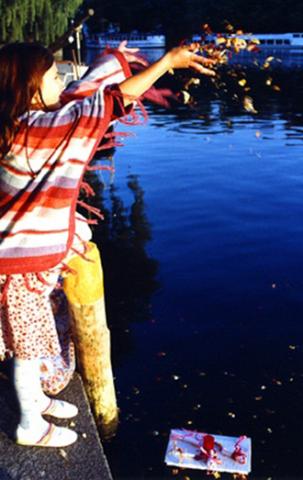 Ein Mädchen wirft Blüten in den Landwehrkanal, wo schon ein selbstgebasteltes Schiffchen schwimmt