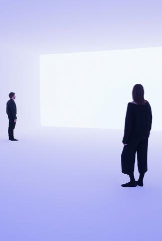 A man and a woman stand in a light blue room and look towards a white rectangle on the wall