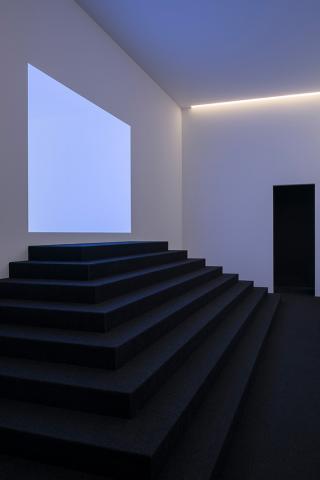 A dark staircase leads towards an empty wall that features a rectangular light field
