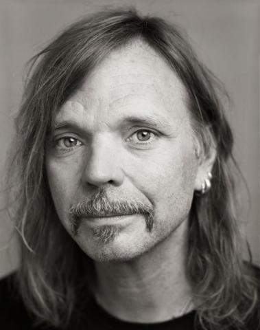 Schwarz-Weiß-Porträtfoto von typex: ein Mann mit langen Haarender blickt in die Kamera.