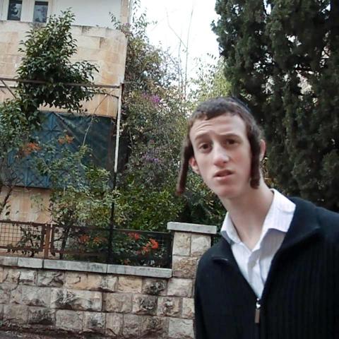 In a Jerusalem residential neighborhood, a young man with payes looks into the camera with a curiously surprised expression.