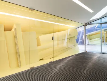 Hinter einer Glaswand liegt ein Stapel überdimensional großer Bücher.