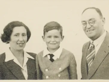 B-W image. Heavily yellowed. A woman, a child and a man in formal dress look friendly into the camera. 