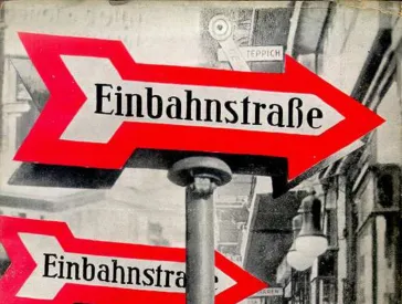 Book cover of One-Way Street by Walter Benjamin: A black-and-white photograph of a street; in the foreground, several traffic signs with a red arrow and the inscription One-Way Street.