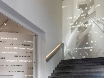 Eine Treppe in der Dauerausstellung. An den Wänden stehen Ortsnamen in hebräischer und lateinischer Schrift.