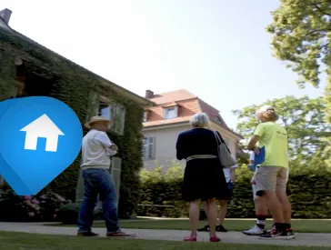 Fünf Menschen stehen vor einer Villa. Am linken Bildrand ist ein Browserfenster mit einem Foto und abgeschnittenen Text zu sehen – daneben ein blauer Pin mit einem weißen Haus-Symbol.