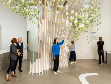 Mehrere Menschen stehen an einem Baum aus Holz. Sie sind in einem Museum
