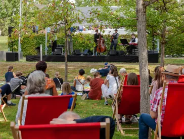 Das Publikum liegt in einem Garten auf Liegest&uuml;hlen und schaut zu einer Musikband, die auf einer B&uuml;hne spielt.