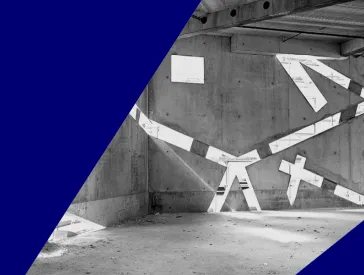 Schwarz-wei&szlig;-Foto eines noch im Bau befindlichen, leeren Raums, in dessen Betonw&auml;nden durch sehr schr&auml;ge Fenster Licht einf&auml;llt.