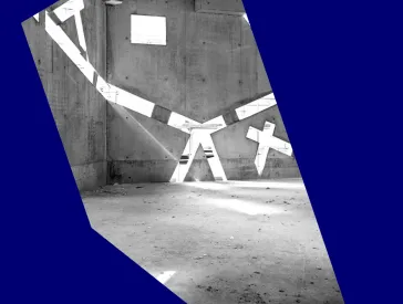 A black-and-white photo of an empty room still under construction, with very slanted windows in its concrete walls through which light streams in.