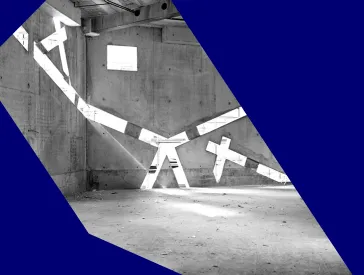 Schwarz-wei&szlig;-Foto eines noch im Bau befindlichen, leeren Raums, in dessen Betonw&auml;nden sehr schr&auml;ge Fenster sind, durch die Licht einf&auml;llt.