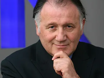 Portr&auml;t eines Mannes, der die Hand ans Kinn h&auml;lt und mit fragendem L&auml;cheln in die Kamera schaut.