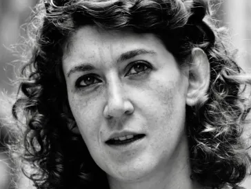 Schwarz-weiß-Porträt einer Frau mit halblangen Locken und Brille im Haar, die nach schräg oben schaut.