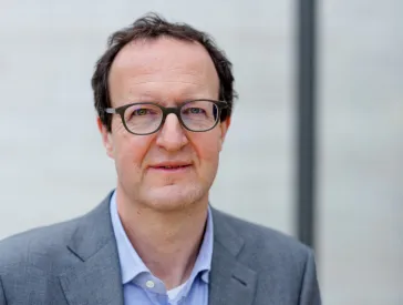 Mann mit Brille schaut freundlich in die Kamera und hat einen Anzug an.