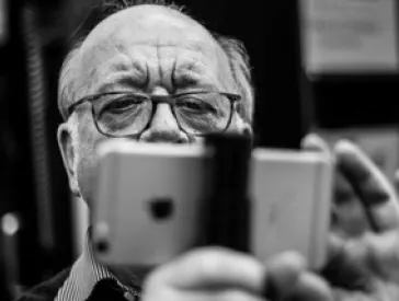 Schwarz-Wei&szlig;-Foto eines Mannes mit Glatze und Brille, der ein iPhone auf einem Stativ festh&auml;lt und damit filmt.