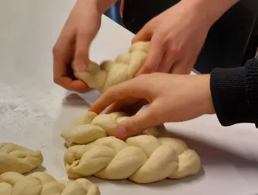 Hände fertigen Teigzöpfe auf einem Tisch an.