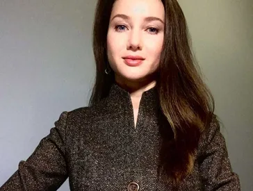 Woman with long black hair and dark jacket looks friendly into the camera.