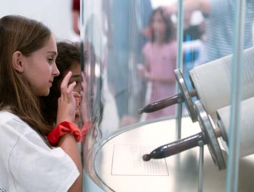 Two children are looking at a Torah scroll that is behind a curved glass panel.