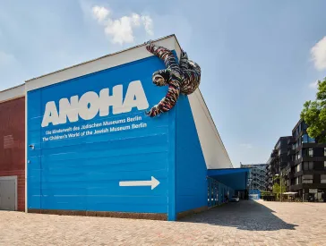 Blaues Gebäude mit Schriftzug, an dem ein Faultier aus Fahrradteilen hängt