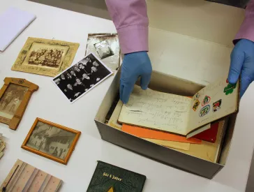 H&auml;nde greifen in einen Karton mit Briefen, Fotos und Dokumenten.