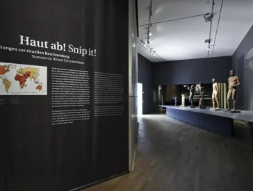 Ausstellungsraum, in dem mehrere nackte m&auml;nnliche Skulpturen auf einem Podest stehen
