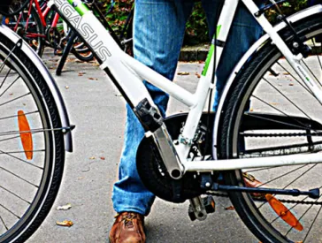 Im Vordergrund der Ausschnitt eines Fahrrads, dahinter steht eine Person. 