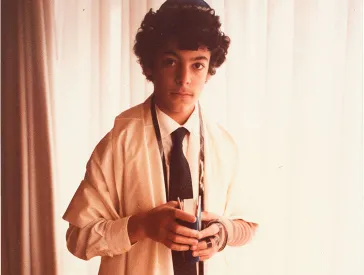 Porträt von Rabin Yaghoubi, der einen Tallit, Tefillin sowie eine Kippa trägt. In seinen Händen hält er ein Gebetbuch.