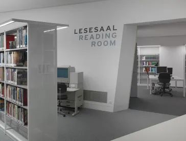 Blick in den Gang zwischen zwei Buchregalreihen in einer Bibliothek.