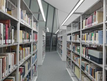Blick in den Gang zwischen zwei Buchregalreihen in einer Bibliothek