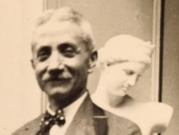 Schwarz-weiß-Porträtfoto eines Mannes (Carl Melchior). Er steht vor der weißen Statue einer Frau, von der der Kopf im Halbprofil und ein Armstumpf zu sehen sind.