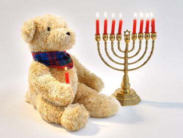 A teddybear holding a burning candle sits alongside an eight-branched lampstand.