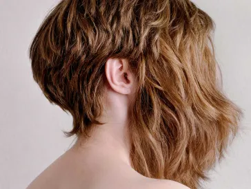 Fotografie einer Frau, die zwei Perücken trägt, eine davon bedeckt ihr Gesicht.