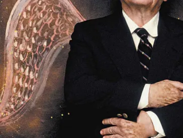 Ein älterer Mann in Anzug und Krawatte mit Engelsflügeln und Heiligenschein schaut mit verschränkten Armen zum Himmel. 