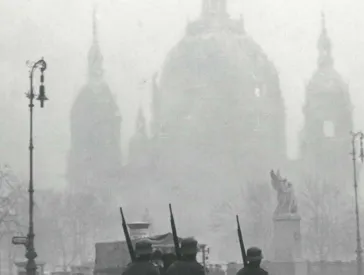 Cover of the catalog for the exhibition “Roman Vishniac’s Berlin”, historical black and white photograph of a small group of troops wearing large coats marching on a foggy day.
