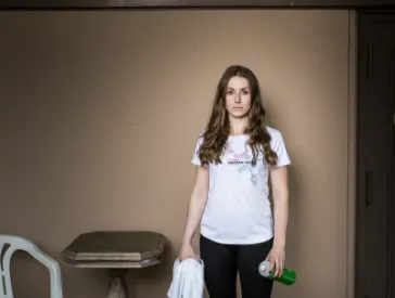 Eine junge Frau in Trikot und 7/8-Hosen und Sportschuhen blickt in die Kamera.