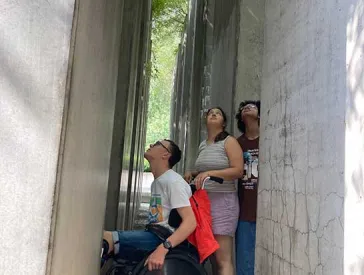 Das Bild zeigt drei Jugendliche zwischen Betonblöcken. sie schauen nach oben. Einer der Jugendlichen sitzt in einem Rollstuhl.