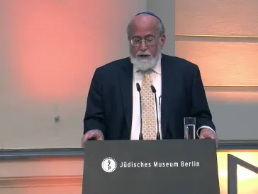 Ein Mann auf einer B&uuml;hne hinter einem Pult h&auml;lt eine Rede.