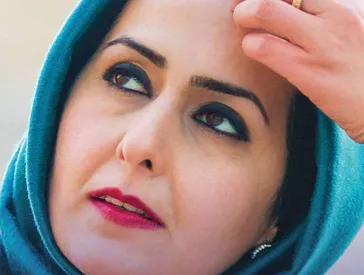 Portrait of a woman with a blue headscarf, lipstick and eye shadow, looking upwards to the left.