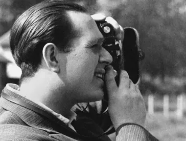 Die Aufnahme zeigt Fred Stein im Seitenprofil beim Fotografieren. Er tr&auml;gt ein Nadelstreifen-Jackett und ein Hemd ohne Krawatte.