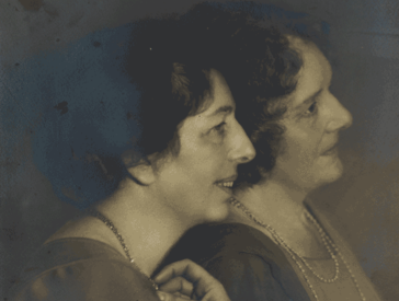 Old picture of two women in profile leaning against each other.