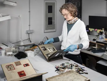 A woman with blue rubber gloves standing at a desk, looking through old pictures.
