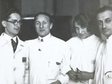 Black-and-white photograph. Erich Simenauer is the second from the left in a group of four. Standing to his right is a woman with a coy expression. Everyone is dressed in white doctor’s coats. None of the three others have been identified.