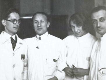Schwarz-Weiß-Foto: Erich Simenauer steht als zweiter von links in einer Gruppe von vier Personen, rechts neben ihm steht eine Frau, die kess in die Kamera schaut, alle tragen weiße Kittel. Keiner der anderen Abgebildeten ist namentlich bekannt.