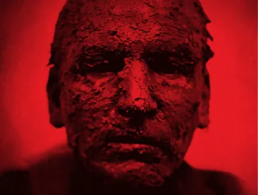 A man with earthy skin looks into the camera, the picture is colored red.