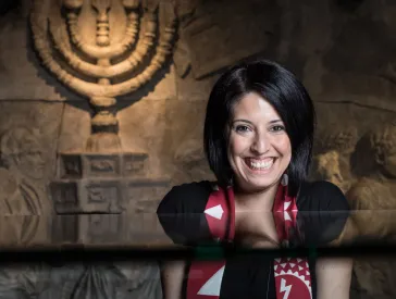 A laughing woman standing in a room of the exhibition “Welcome to Jerusalem”