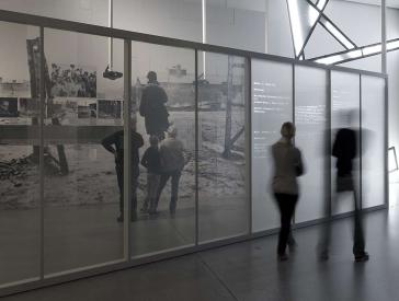 Visitors walk by in a blur while reading text on a wall in the permanent exhibition.