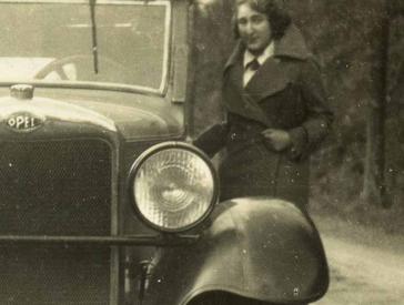 Black and white photo of a young woman in winter clothes next to a car on a country road.