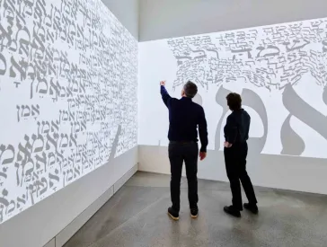 Large canvas with Hebrew letters in front of which two people stand