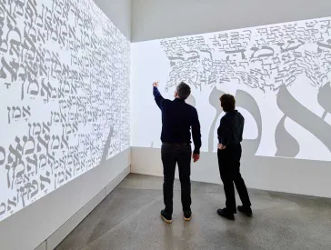 Large screen with Hebrew letters in front of which two people are standing.