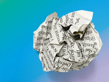 Zerknülltes, bedrucktes, zu einer Kugel geformtes Stück Papier, vor einem Hintergrund mit gelb-blau-grün-lila Farbverlauf.